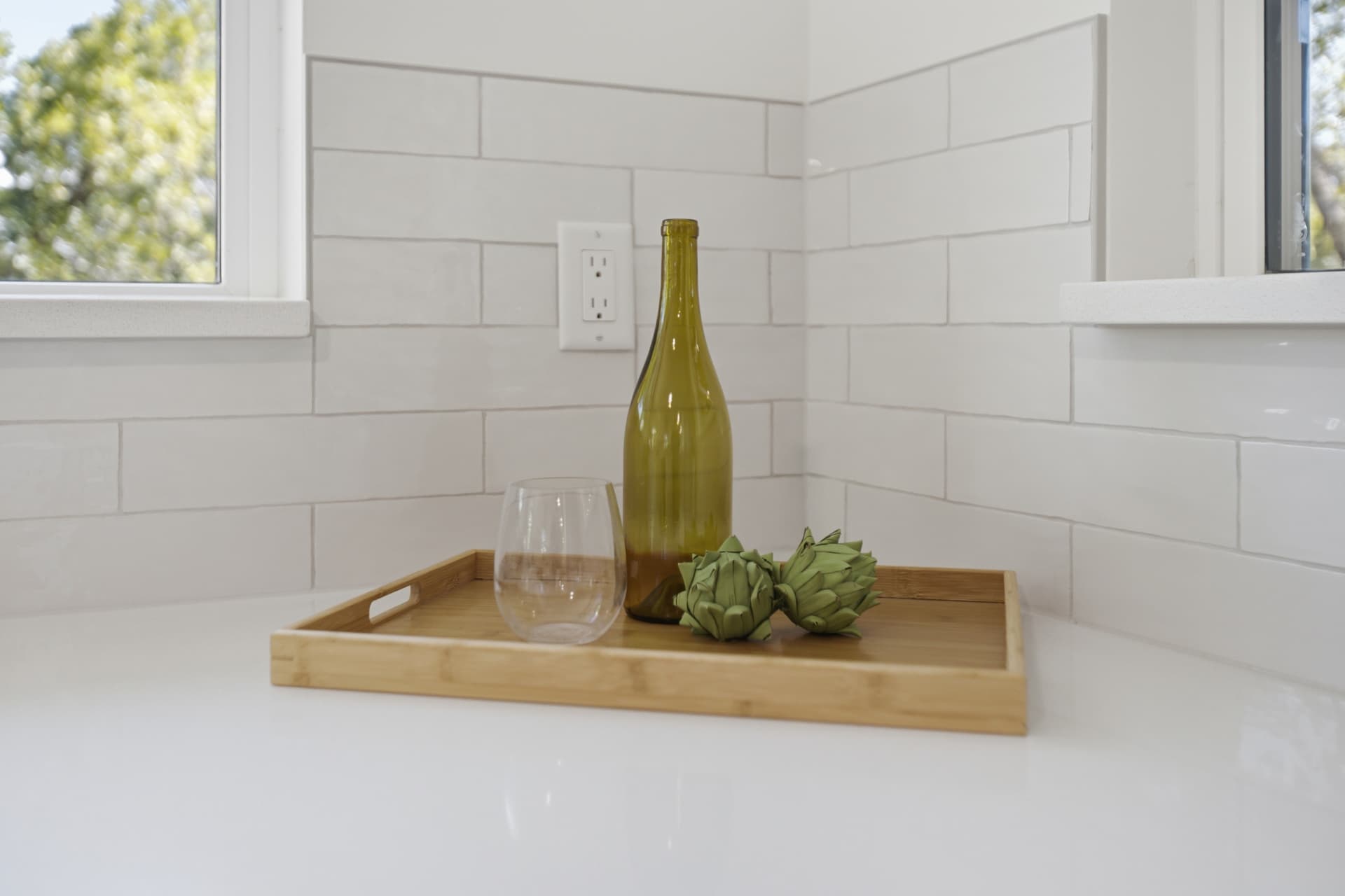 Wood tray with wine bottle and stemless glass on white quartz counter against subway tile backsplash