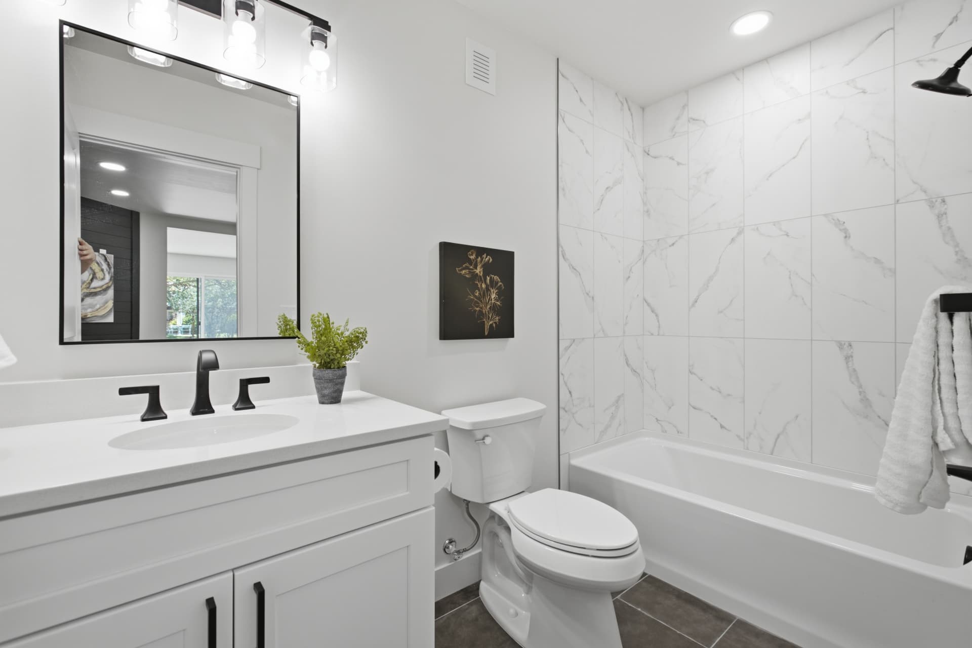 Guest bathroom with white vanity, black fixtures, framed mirror, and marble-look tiled tub surround