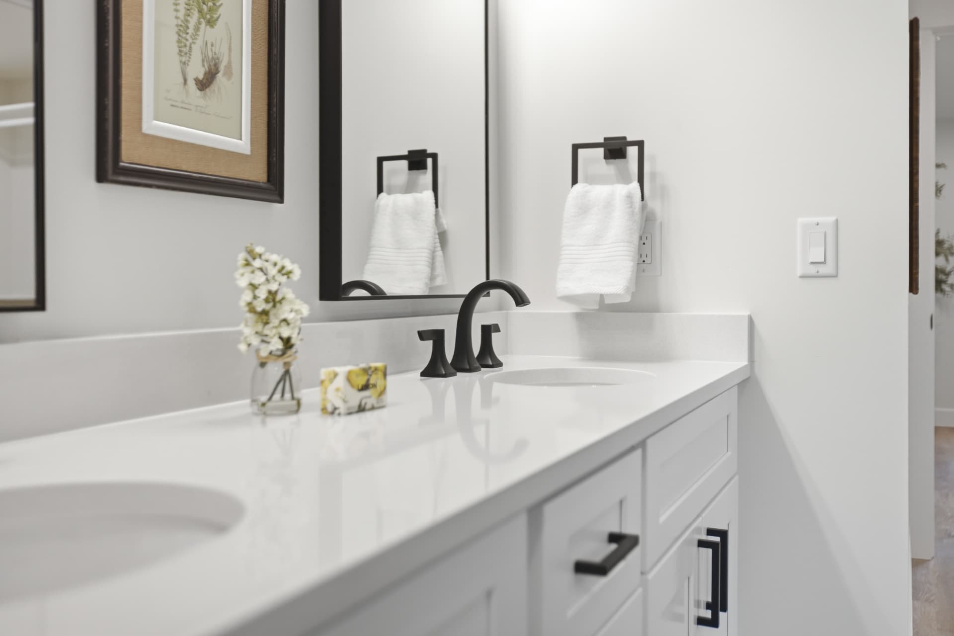 White double vanity with quartz counter, black fixtures, and framed mirrors