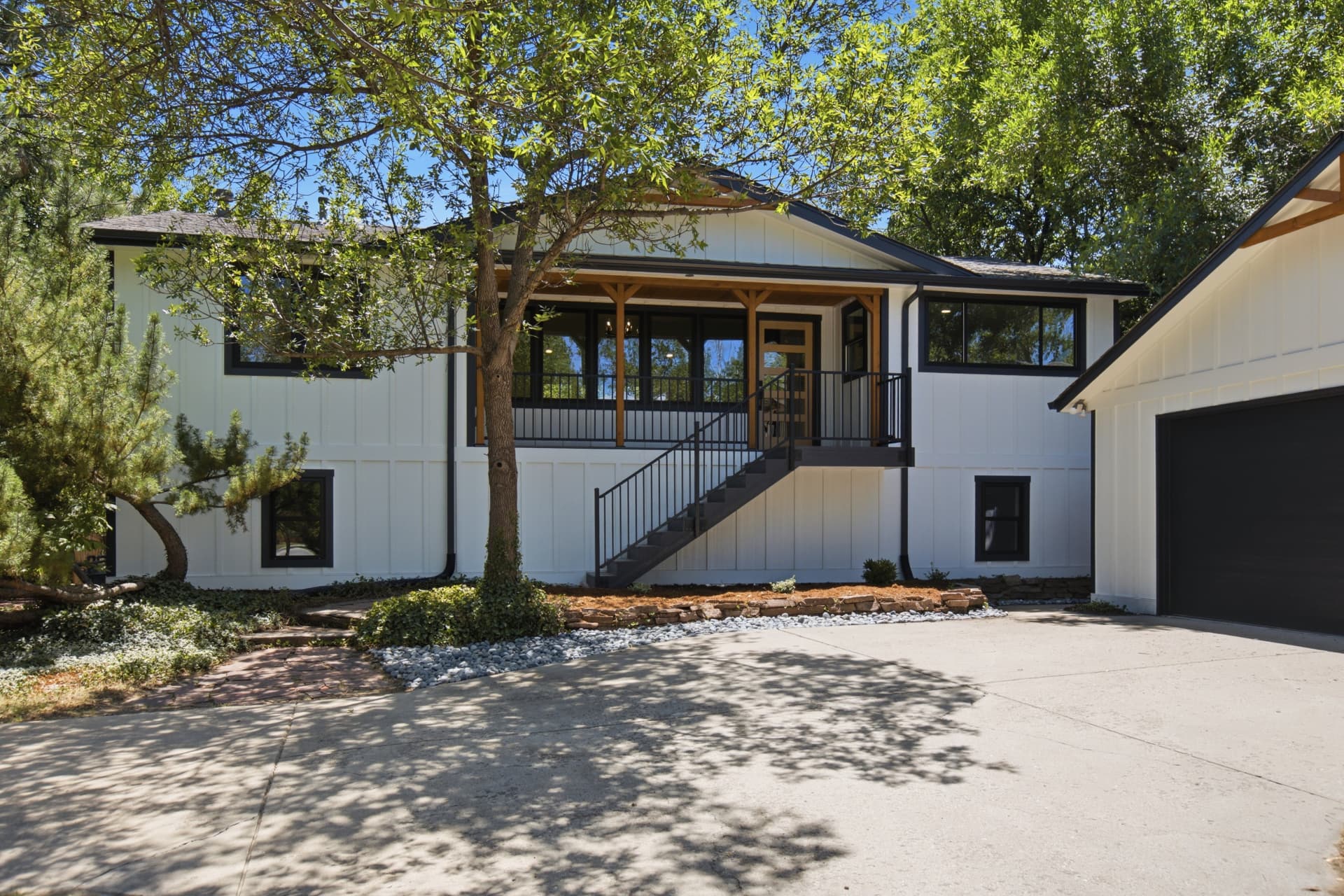 White board-and-batten farmhouse exterior with covered porch, black trim, and mature shade trees