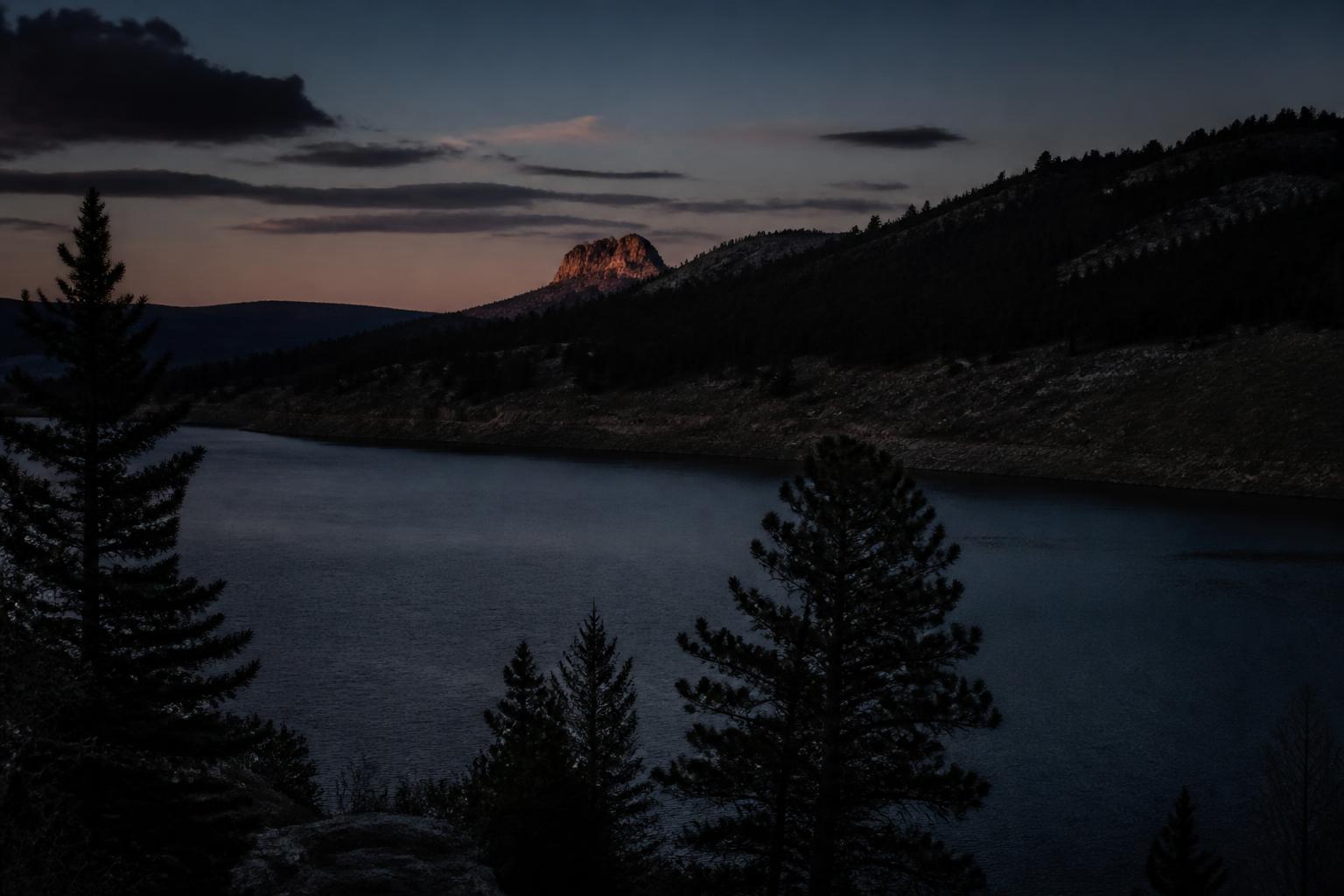 Painted illustration of Larimer County, Colorado, with Horsetooth Rock in silhouette above a still reservoir holding a band of gold reflection at sunset.