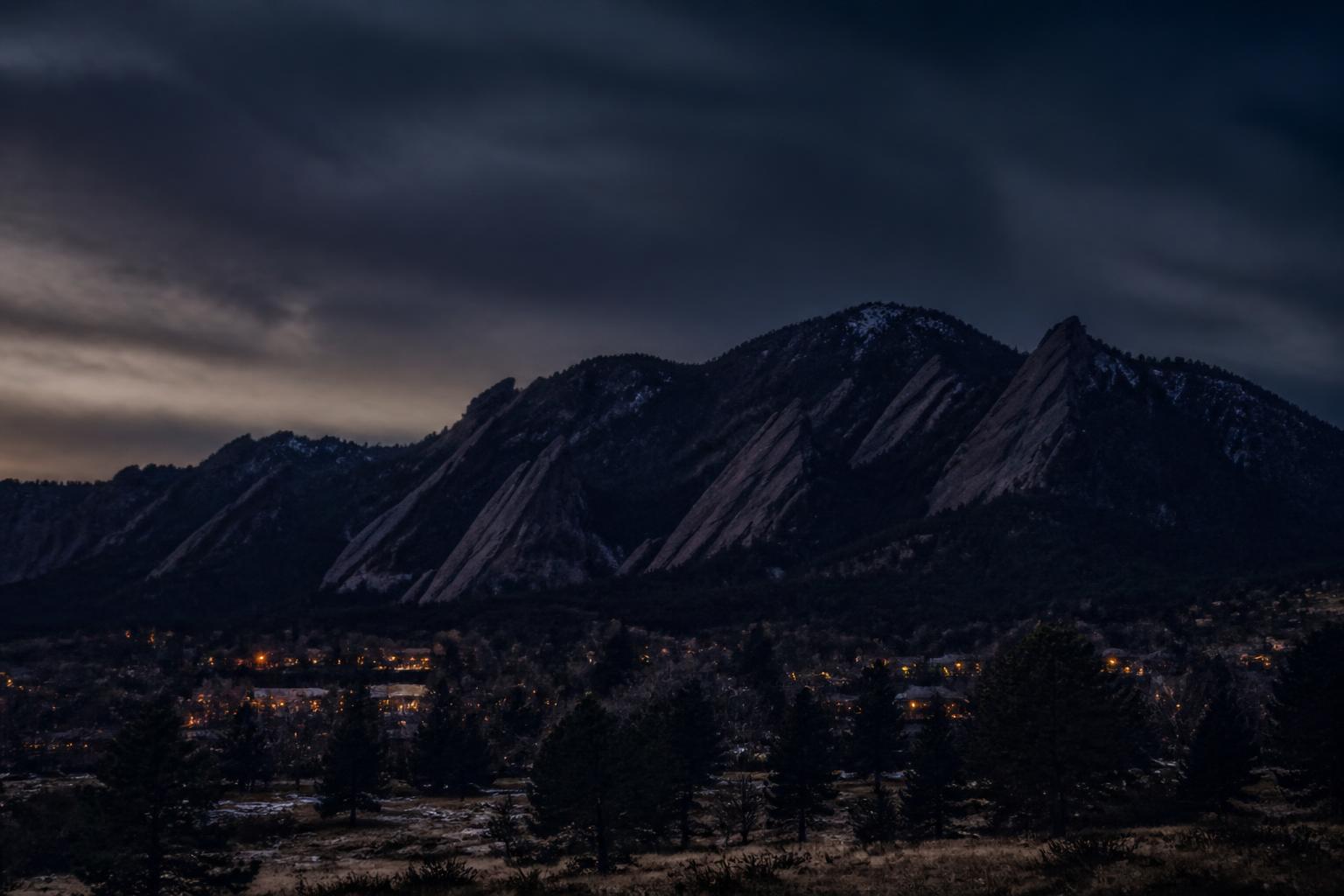 Painted illustration of Boulder County, Colorado, with the Flatirons catching the last warm light above dark massed ponderosa pines.