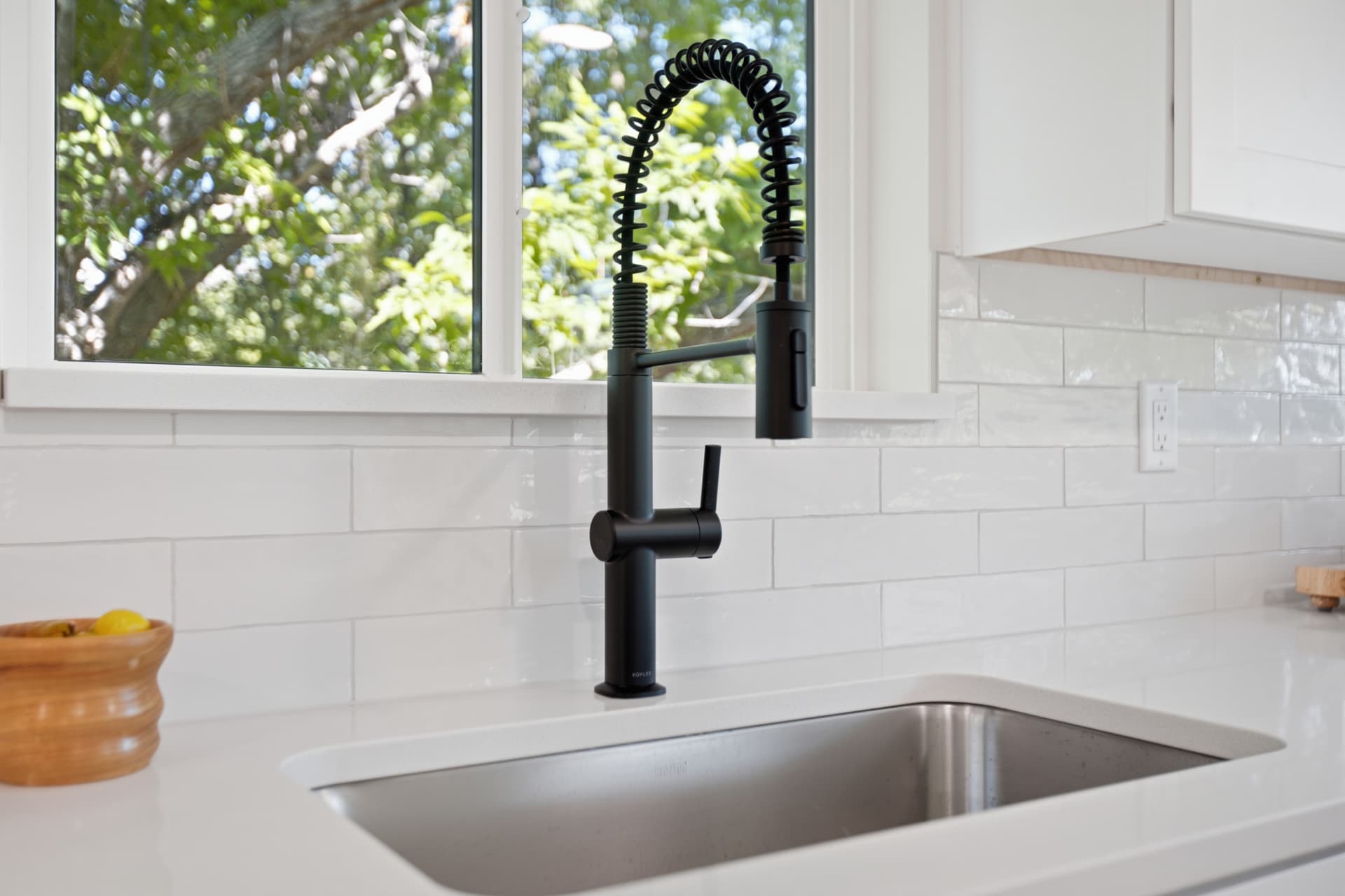 Matte black spring kitchen faucet over undermount stainless sink beside a sunlit window
