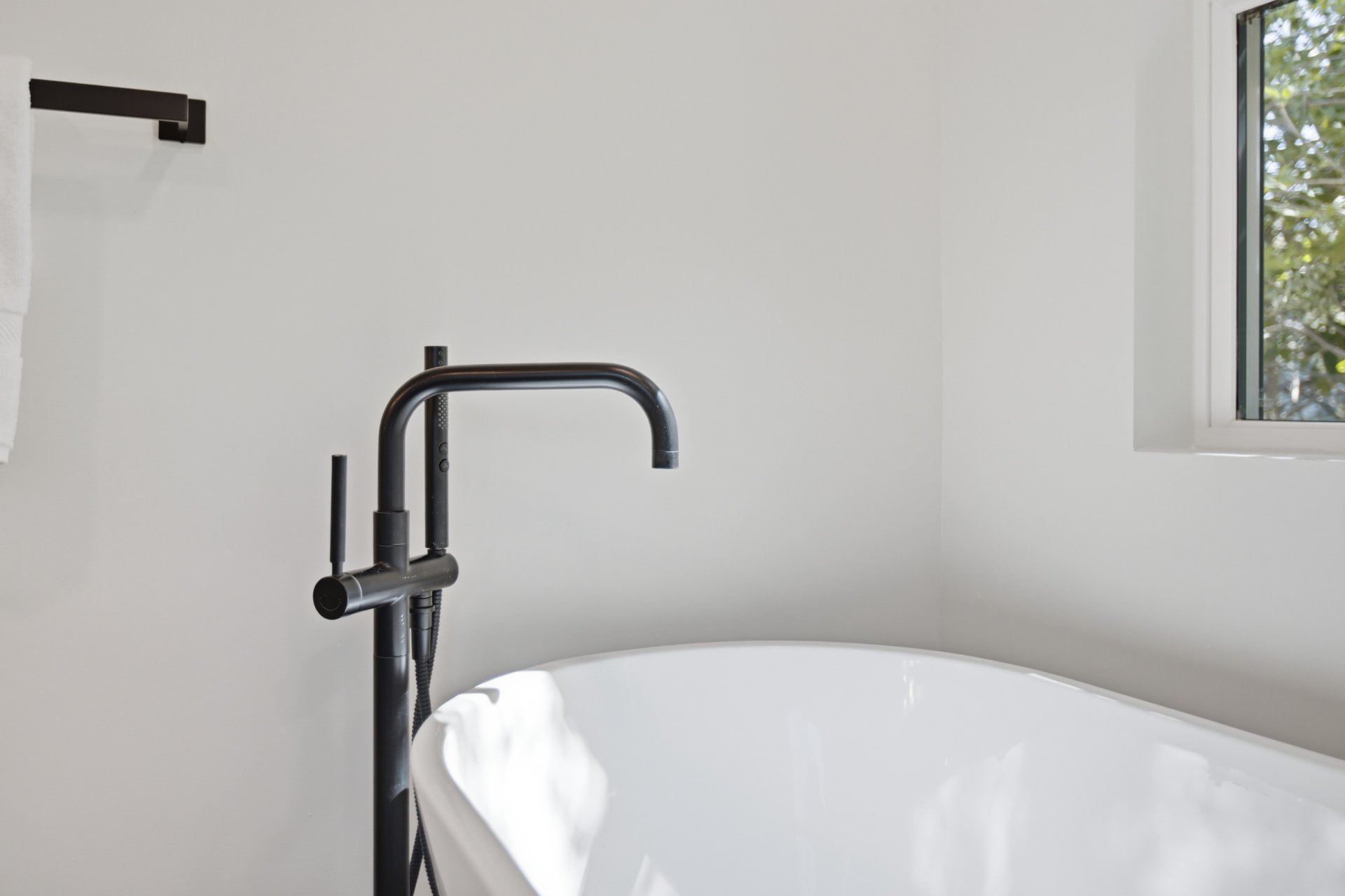 Freestanding white soaking tub with matte black floor-mounted tub filler